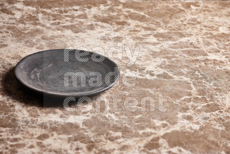 A circular black pottery plate on beige marble background