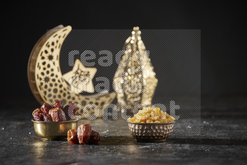 Dates in a metal bowl with raisins beside golden lanterns in a dark setup