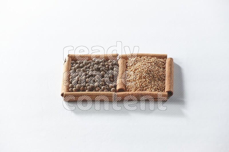 مربعان من أعواد القرفة ممتلئان بحبوب الخردل وحبوب بهار الفلفل الحلو علي خلفية بيضاء