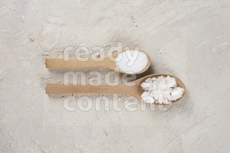 2 wooden spoons filled with fine and coarse salt on white background