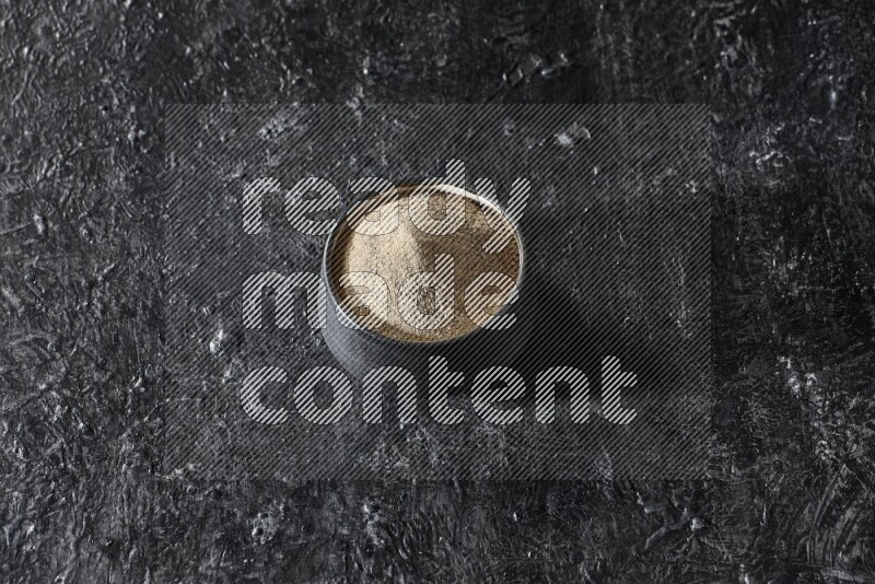 وعاء فخار أسود مملوء ببودرة الفلفل الأبيض على أرضية سوداء