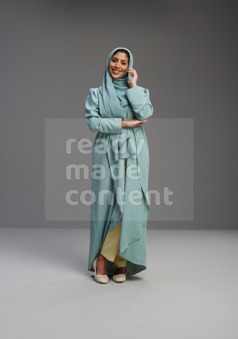 Saudi Woman wearing Abaya standing talking on phone on Gray background