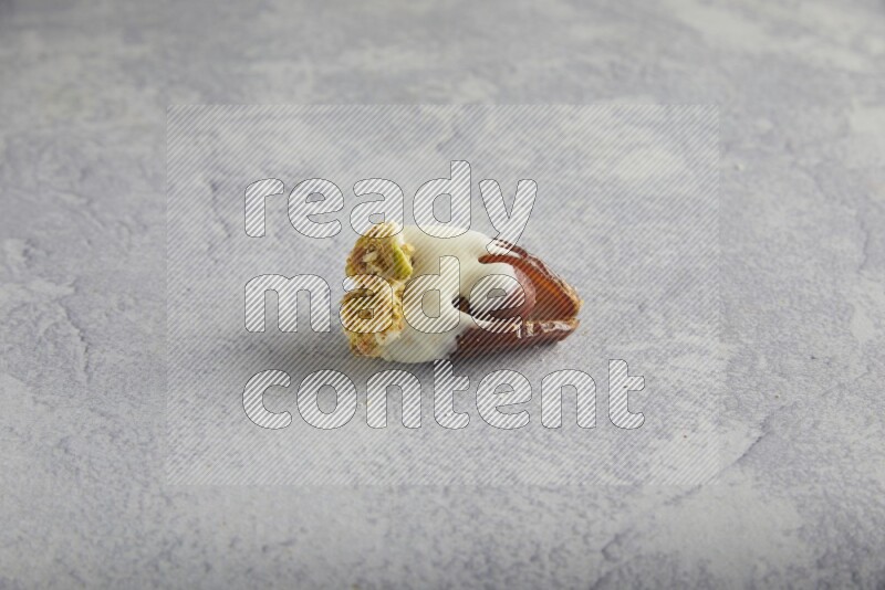 Hazulnut stuffed date covered with white chocolate and crushed peanuts & pistachios on light grey background