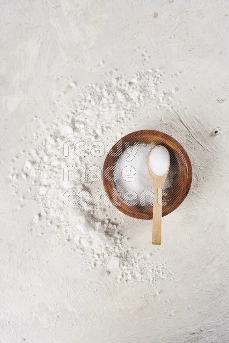 A pottery plate full of fine salt with bunch of coarse salt beside it on white background