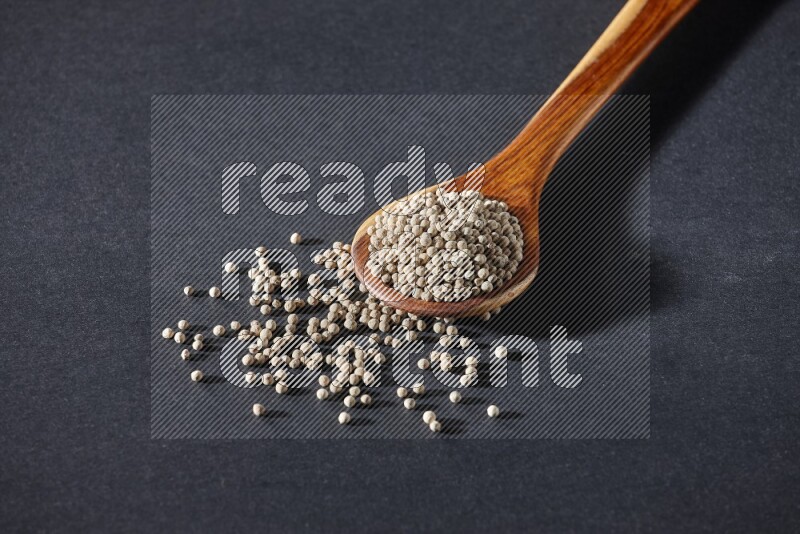 A wooden ladle full of white pepper beads on black flooring