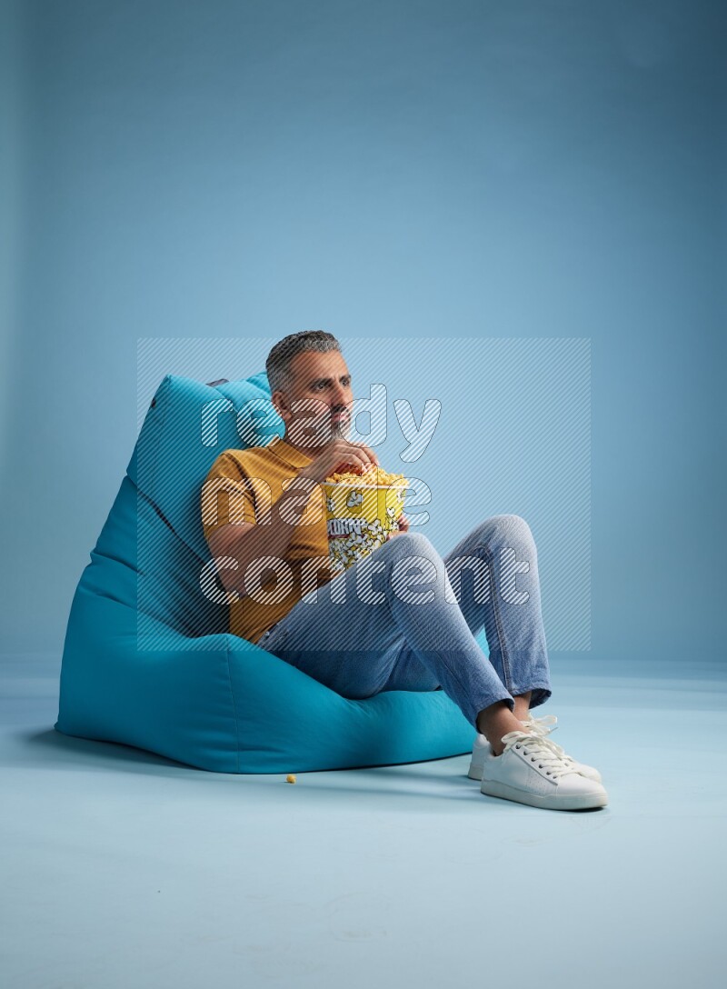 A man sitting on a blue beanbag and eating popcorn