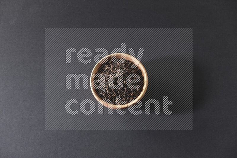 A wooden bowl full of cloves on a black flooring