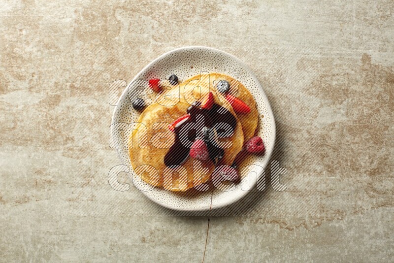 Three stacked mixed berries pancakes in an irregular plate on beige background