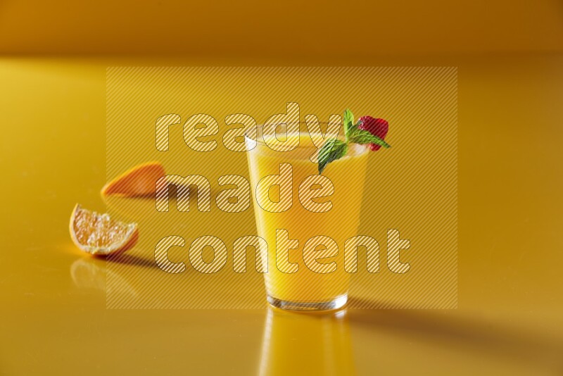glass of orange juice with berry & mint on yellow background