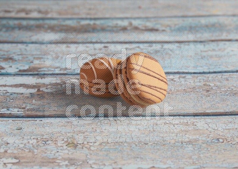 45º Shot of of two assorted Brown Irish Cream, and light brown Almond Cream macarons next to each other on light blue background