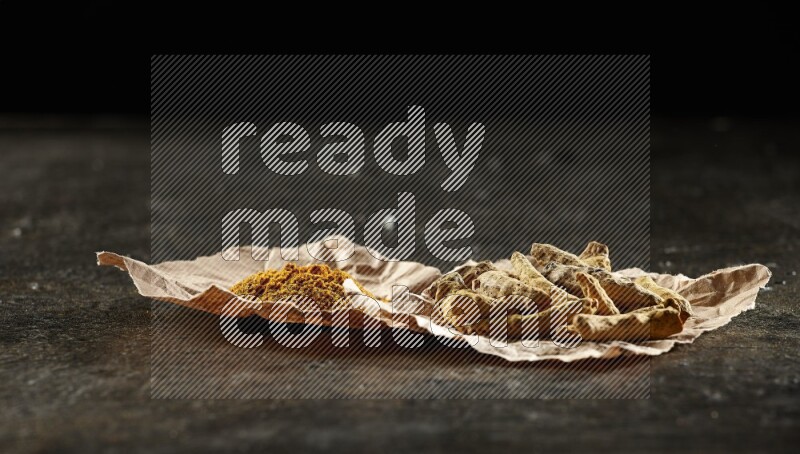 أصابع الكركم المجففة وبودرة الكركم في قطع من الورق على خلفية سوداء