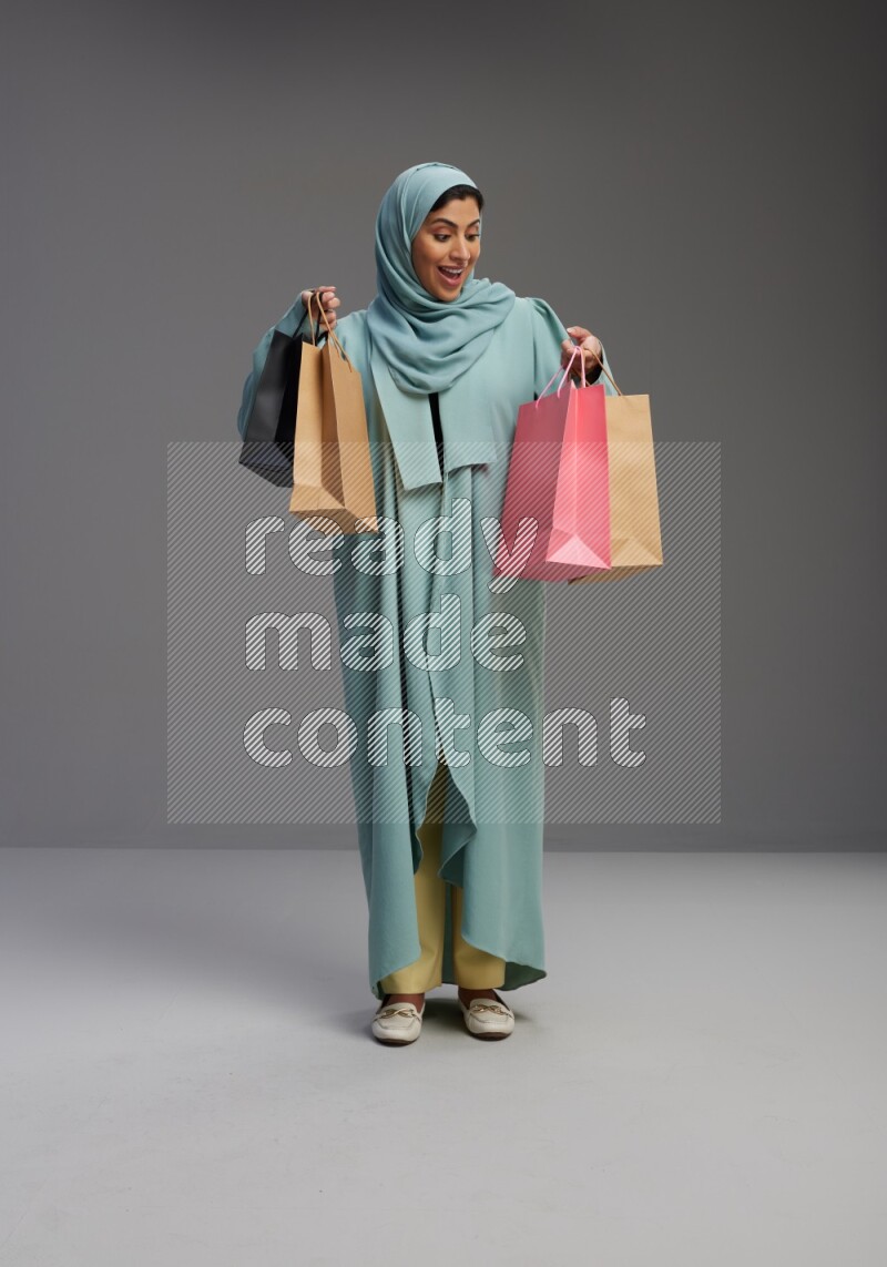 Saudi Woman wearing Abaya standing holding shopping bag on Gray background
