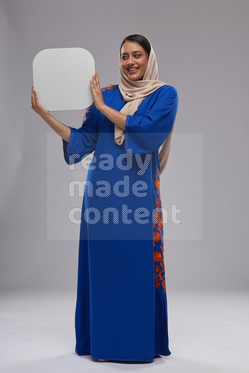 A Saudi woman standing wearing Jalabeya holding a social media sign