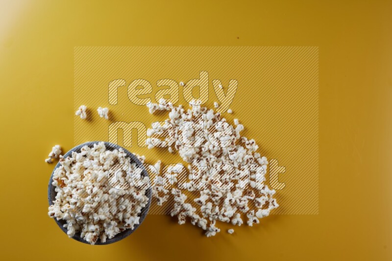 A multicolored pottery bowl full of popcorn with popcorn beside it on a yellow background in different angles