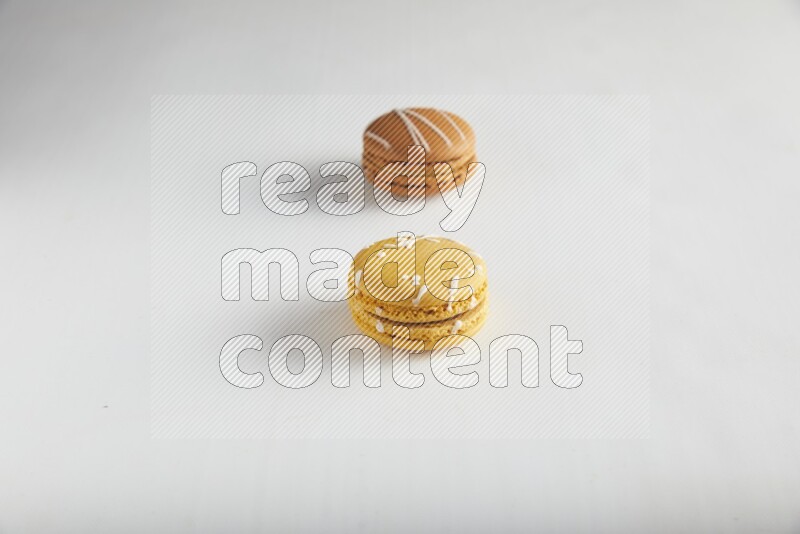 45º Shot of of two assorted Brown Irish Cream, and Yellow Piña Colada macarons on white background