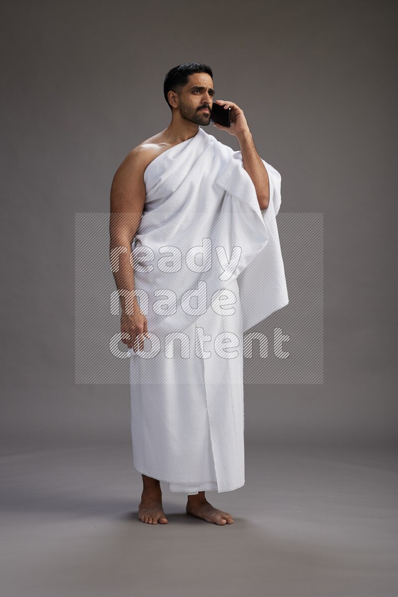 A man wearing Ehram Standing talking on phone on gray background