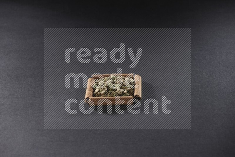 أربعة من أعواد القرفة مكونة شكل مربع بداخلها حبوب الهيل علي خلفية سوداء