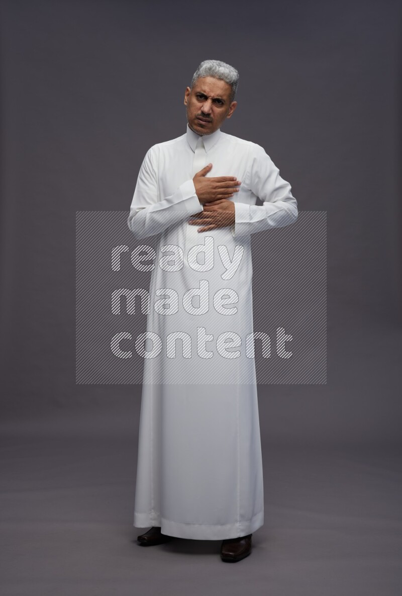 Saudi man wearing thob standing interacting with the camera on gray background