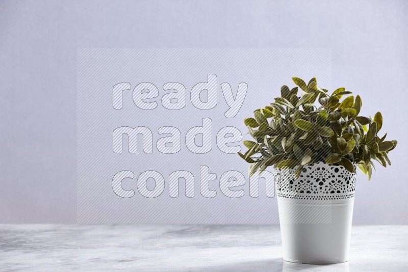 Green artificial plant in white decorative pot on grey marble background