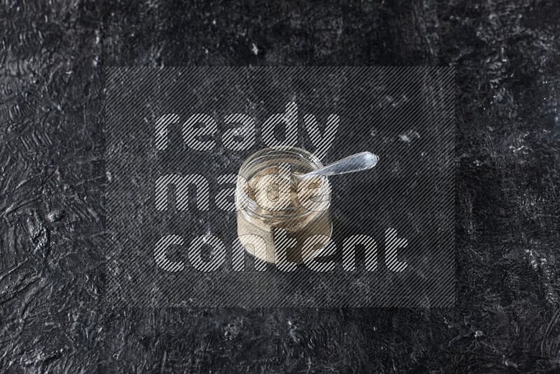 وعاء زجاجي وملعقة معدنية ممتلئان ببودرة الفلفل الأبيض على أرضية سوداء