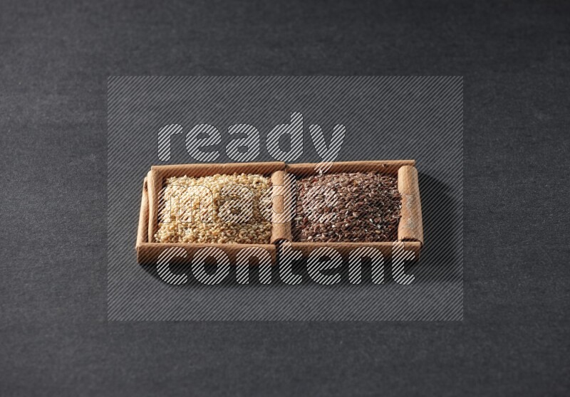 مربعان من أعواد القرفة ممتلئان ببذور الكتان وبذور السمسم علي خلفية سوداء