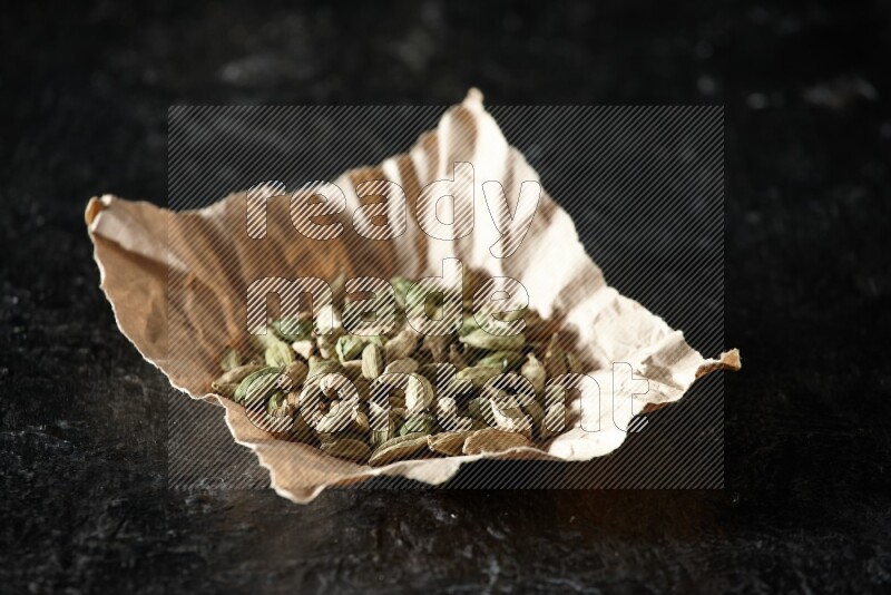 Cardamom seeds in a crumpled piece of paper on textured black flooring
