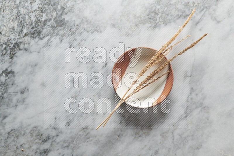 Wheat stalks on multicolored pottery plate on grey marble background