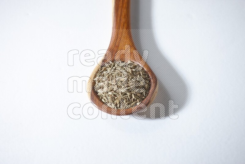 A wooden ladle full of cumin seeds on a white flooring