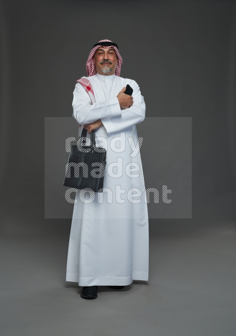 Saudi man with shomag Standing holding bag and phone on gray background