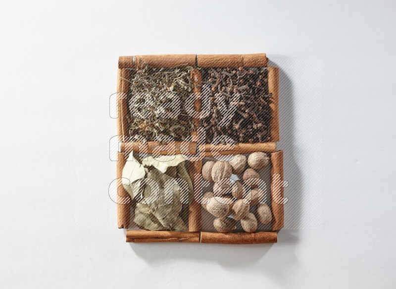 4 مربعات من أعواد القرفة ممتلئة بأوراق الغار والريحان المجفف والقرنفل وجوزة الطيب على أرضية بيضاء