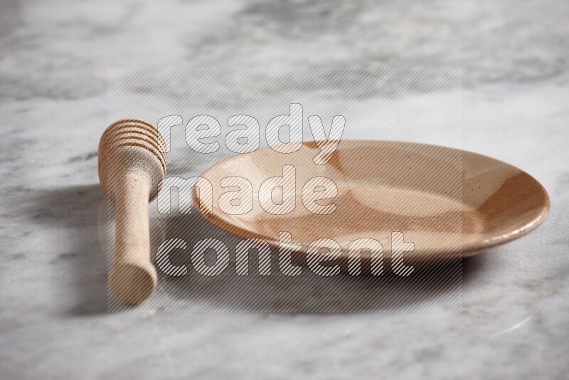 Multicolored pottery plate with wooden honey dipper on the side on grey marble background