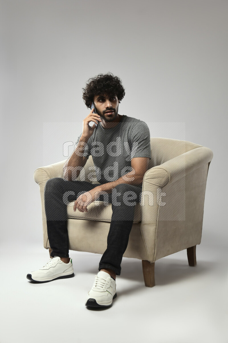 A man wearing casual sitting on a chair talking on the phone on white background