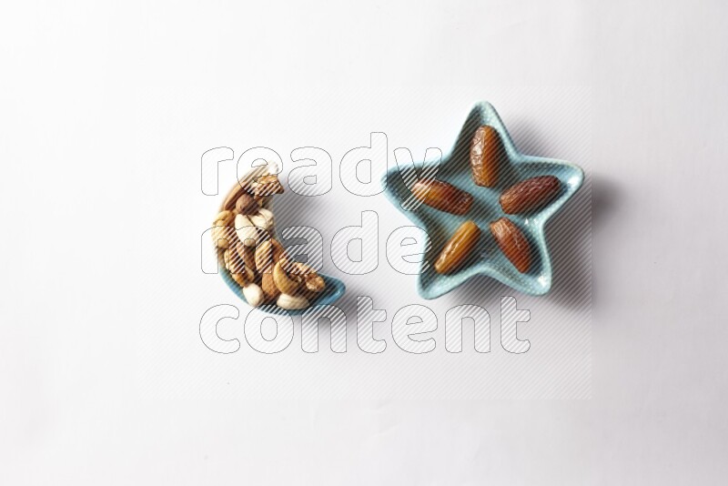 Dates in a star shaped pottery plate and a crescent plate with mixed nuts on white background