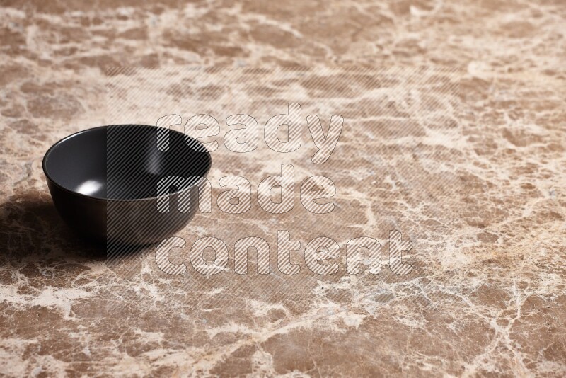 A black ceramic bowl on beige marble background