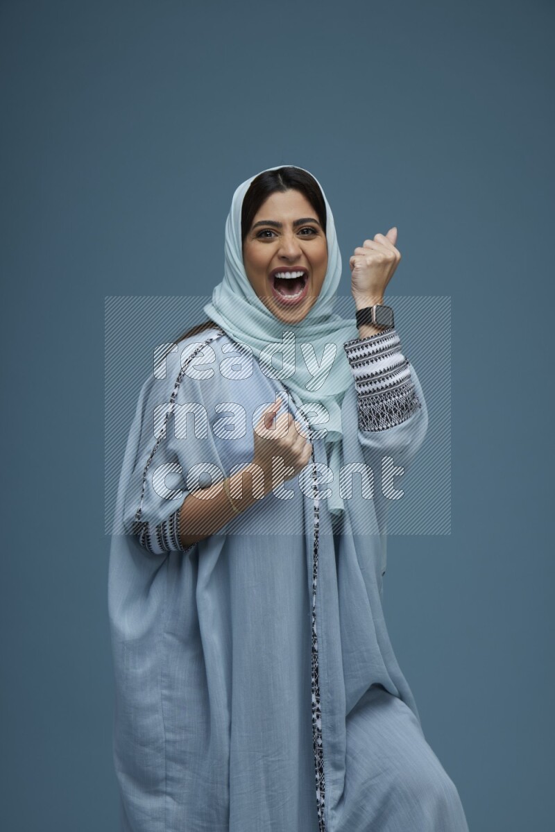 A woman posing in a blue background wearing a blue Abaya with hijab