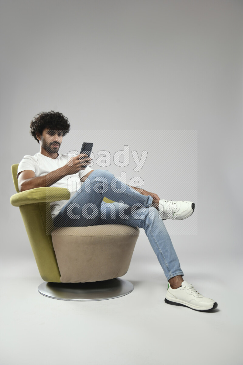 A man wearing casual sitting on a chair browsing on the phone on white background