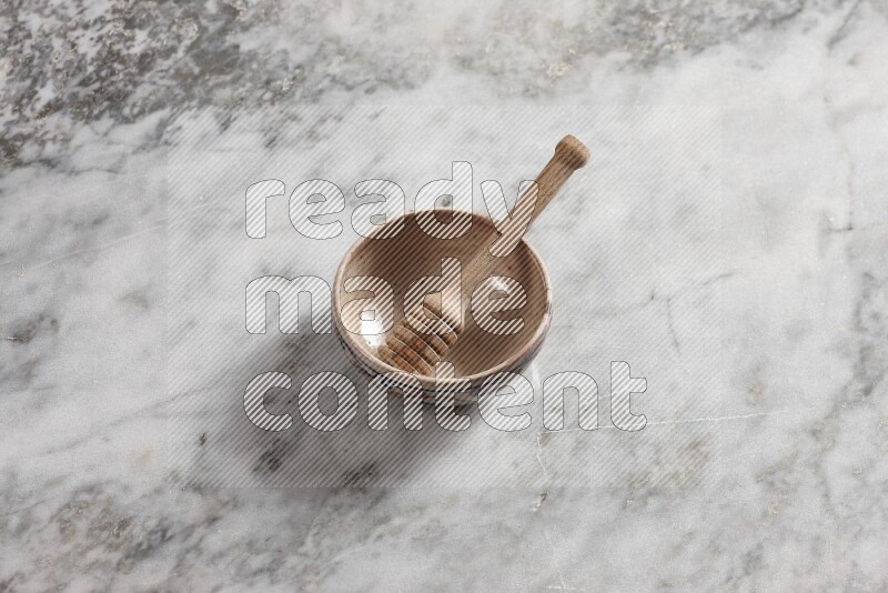 Decorative pottery bowl with wooden honey dipper in it on grey marble background