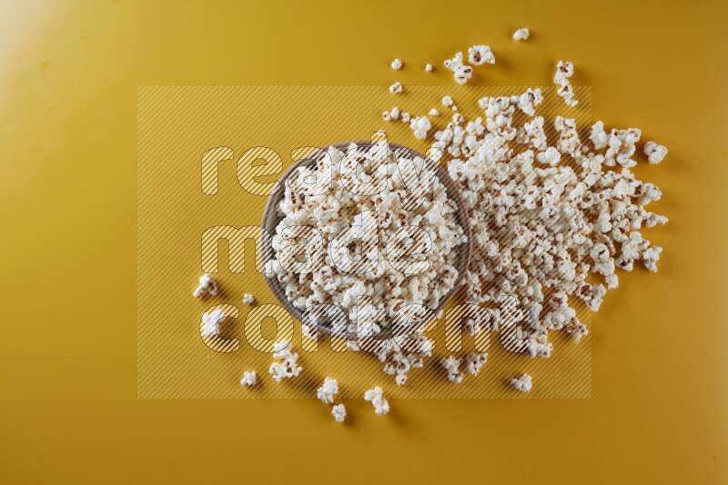 A brown pottery bowl full of popcorn with popcorn beside it on a yellow background in different angles
