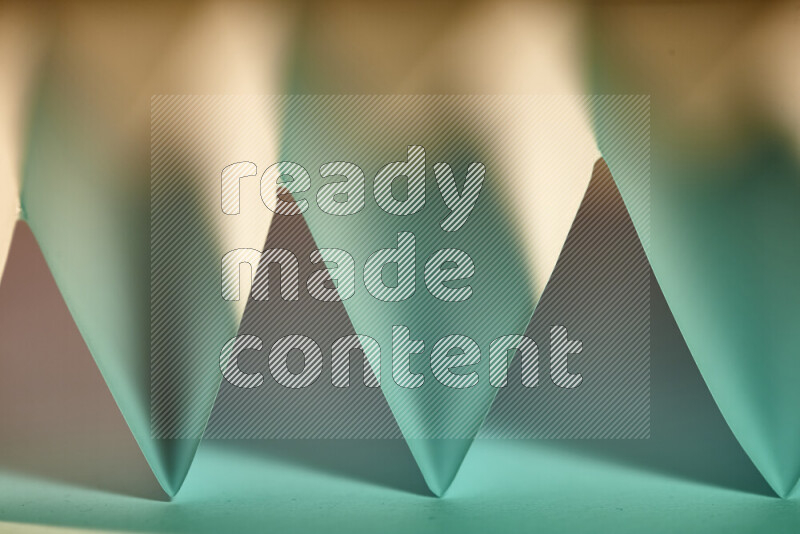 A close-up abstract image showing sharp geometric paper folds in green gradients and warm tones