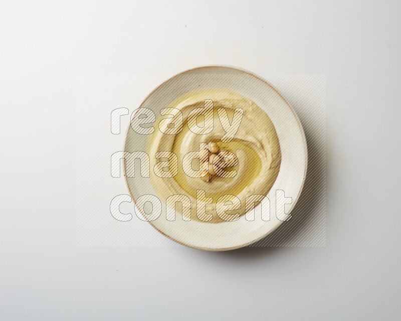Hummus in a pottry plate garnished with roasted chickpeas on a white background