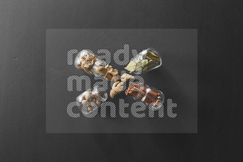 4 glass spice jars full of laurel bay leaves, ginger, cinnamon and nutmeg on black flooring