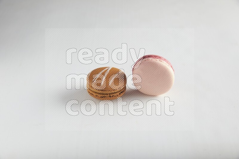 45º Shot of of two assorted Brown Irish Cream, and Pink Litchi Raspberry macarons on white background