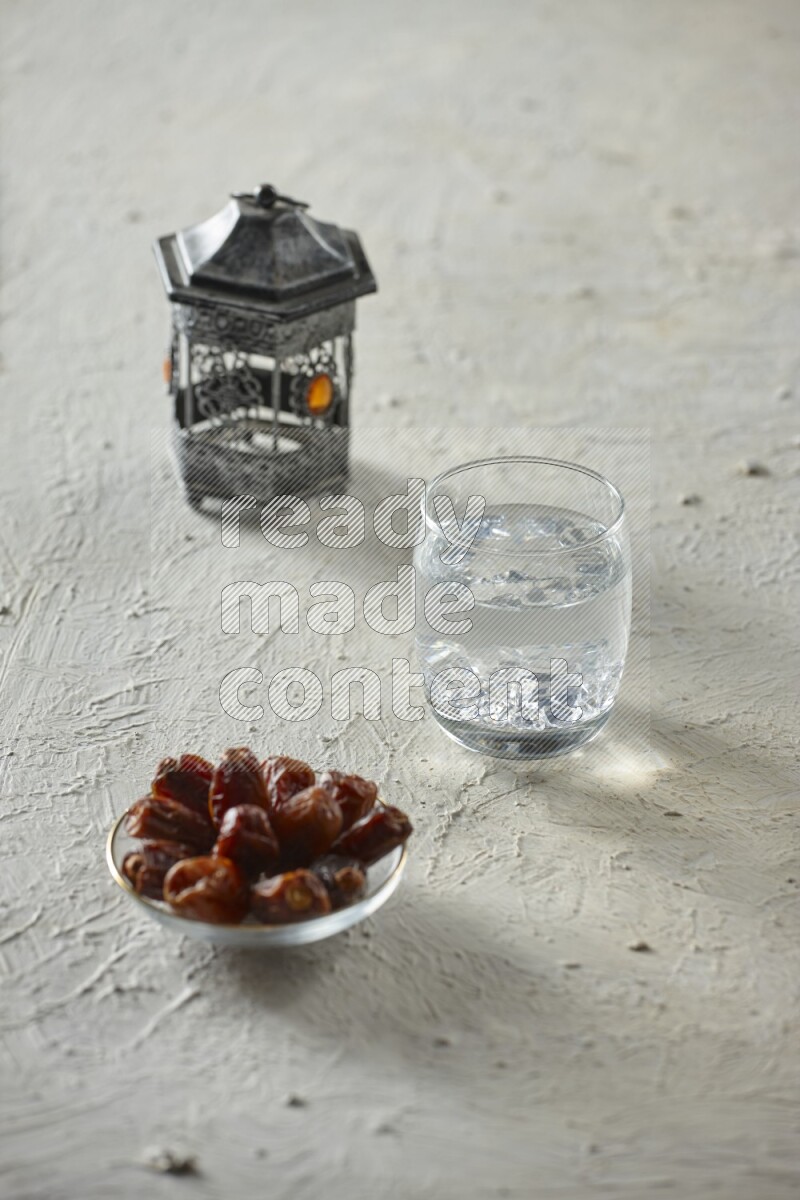 A silver lantern with different drinks, dates, nuts, prayer beads and quran on textured white background