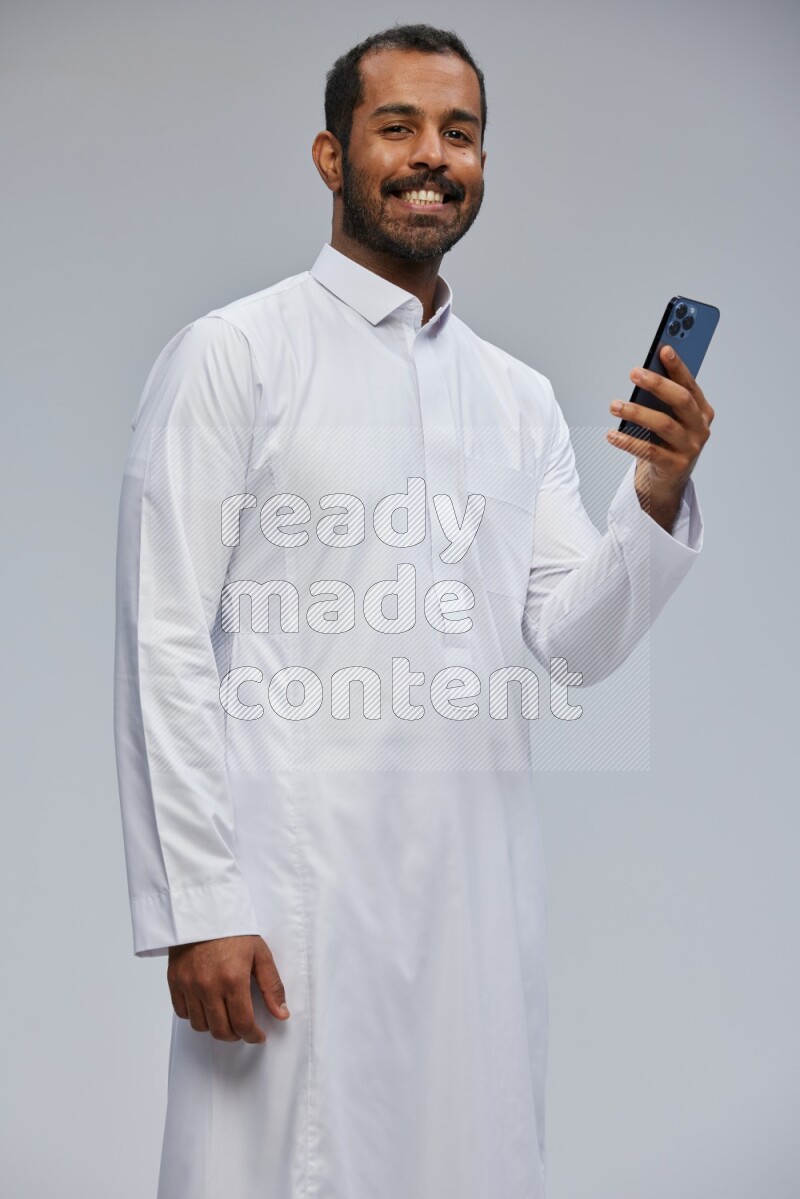 Saudi man wearing Thob standing texting on phone on Gray background