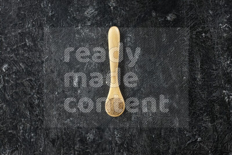 ملعقة خشبية ممتلئة ببودرة الكمون على خلفية سوداء