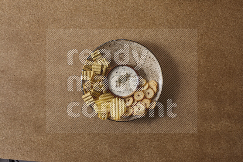 Assorted snacks on a pottery plate with a dipping on brown background