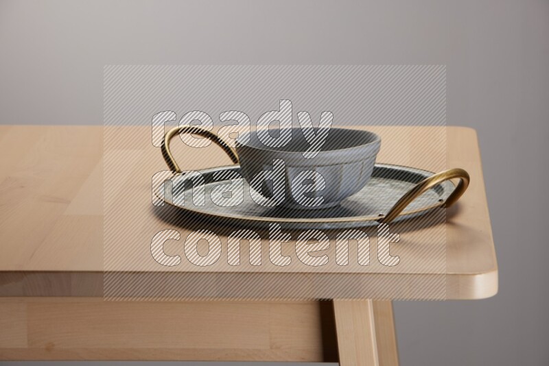 grey bowl placed on a rounded stainless steel tray with golden handels on the edge of wooden table