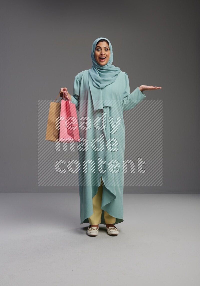 Saudi Woman wearing Abaya standing holding shopping bag on Gray background