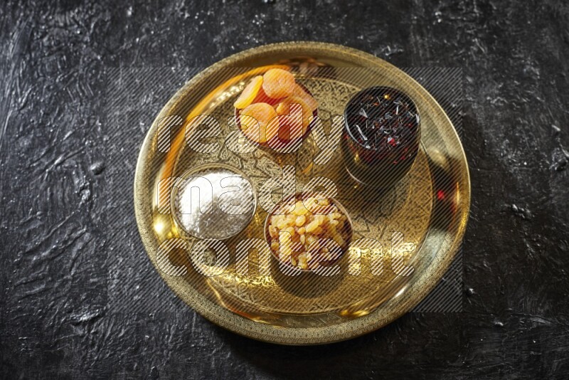 Dried fruits in metal bowls with tamarind on a tray in dark setup