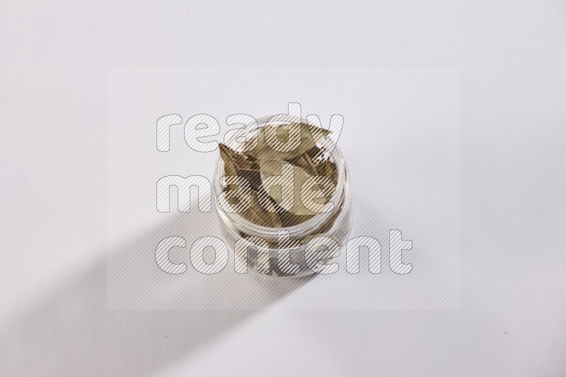 A glass jar filled with dried bay leaves on white flooring